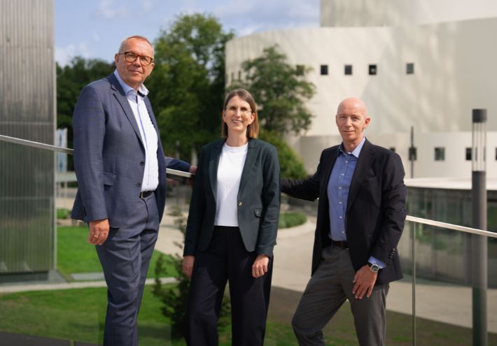 Axel Deitermann, Stefanie Zimmermanns und Michael Pütter von Hotel Affairs Consulting vor modernen Gebäuden im Freien.